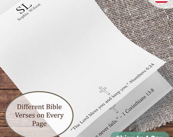 May include: A white stationery notepad featuring the monogram SL and the name Sophia Wilson at the top. Each page includes a small cross icon and a printed Bible verse, specifically Numbers 6:24 and 1 Corinthians 13:8, in black text.