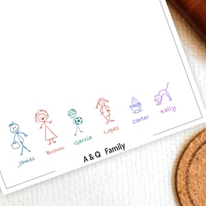 May include: A white notepad with colorful stick figure illustrations of a family, each labeled with a name. The text "A & Q Family" is printed at the bottom. A brown leather wallet and a cork coaster are in the background.