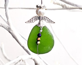 Pode incluir: Enfeite de anjo artesanal com corpo de vidro do mar verde, asas prateadas e cabeça de pérola. O anjo é adornado com uma auréola prateada e uma fileira de contas coloridas. O enfeite pende de um fio de prata.
