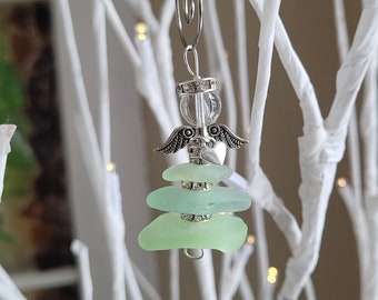 Pode incluir: Enfeite decorativo com um anjo prateado, contas transparentes e pequenas asas. Abaixo, três peças de vidro do mar verde claro. O enfeite é pendurado em um clipe prateado, ideal para uma árvore de Natal.