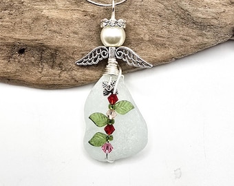 Pode incluir: Pingente de anjo artesanal com cabeça de pérola perolada, asas prateadas e corpo de vidro do mar. O pingente é adornado com contas vermelhas e rosa e detalhes de folhas verdes. O colar é pendurado em uma corrente de prata.