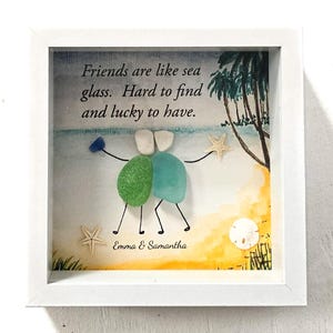 May include: A framed artwork featuring a beach scene with the text "Friends are like sea glass. Hard to find and lucky to have." Two figures made of sea glass are embracing. The artwork includes starfish and a white frame.