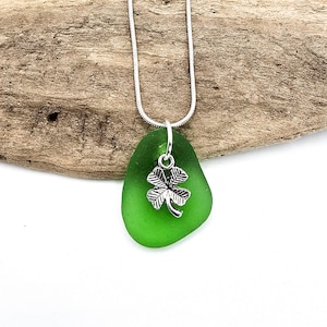 May include: A green sea glass pendant necklace with a silver four-leaf clover charm.