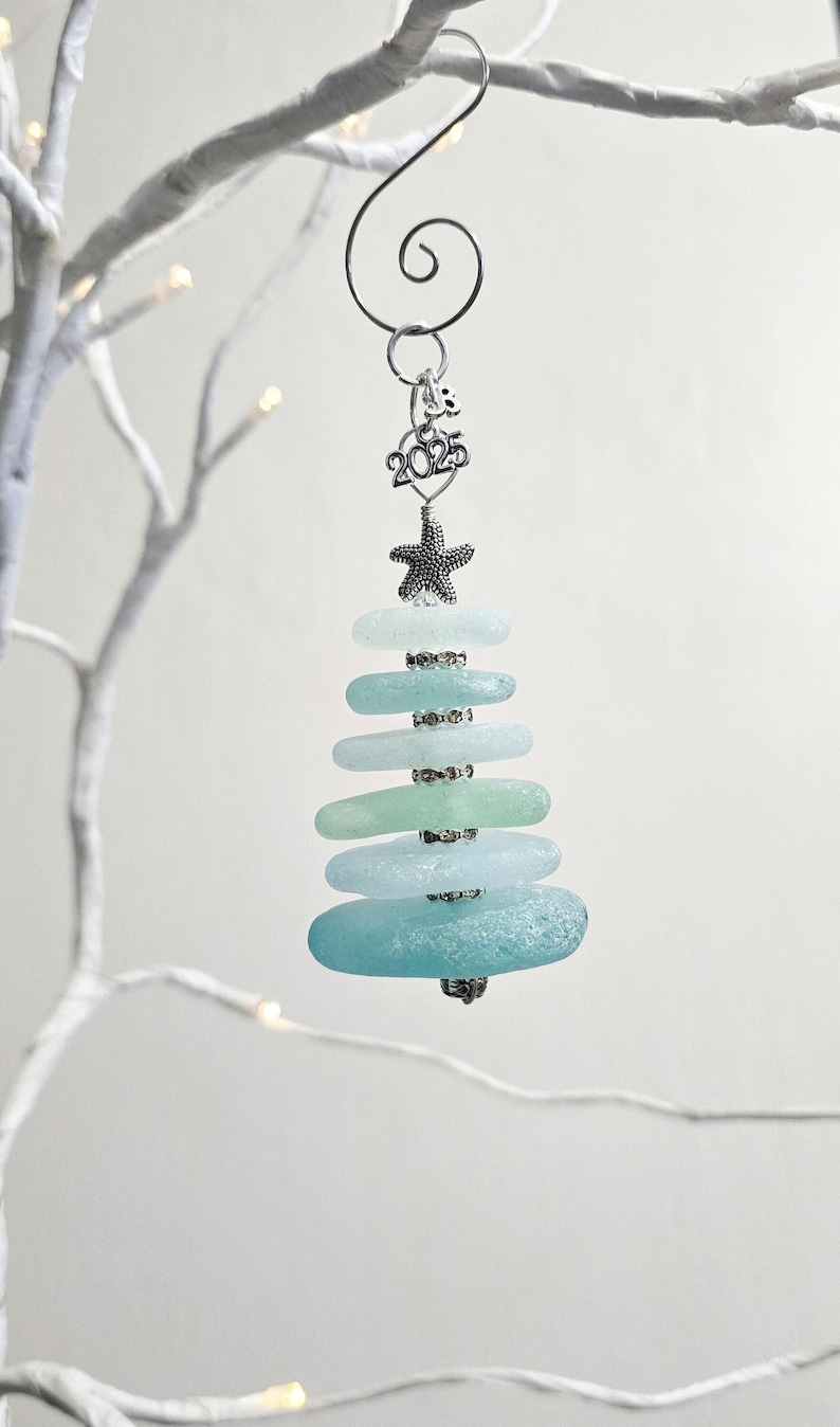 May include: Sea glass Christmas tree ornament featuring a starfish and a 2025 charm. The ornament is made from layered sea glass in shades of blue and green.