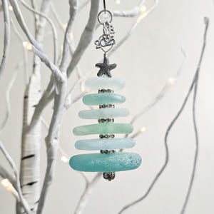 May include: A teal and blue sea glass Christmas tree ornament with a silver starfish and the year 2023 charm.