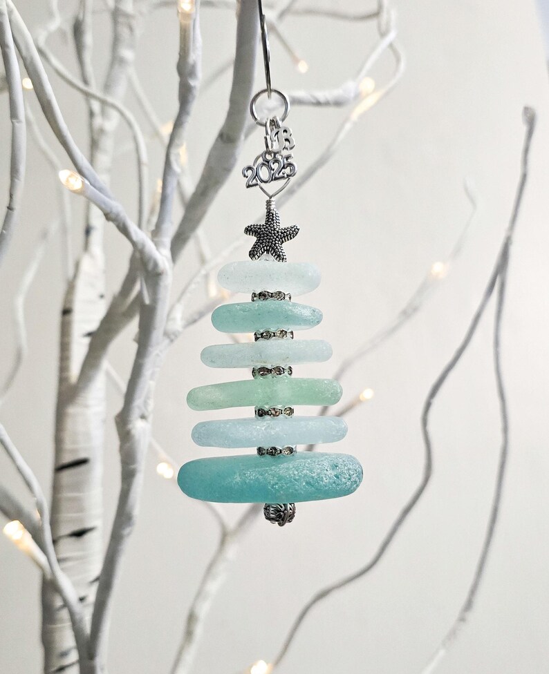 May include: A teal and blue sea glass Christmas tree ornament with a silver starfish and the year 2023 charm.