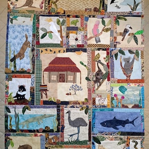 Pode incluir: Um edredom artesanal com vários animais e paisagens australianas. O edredom apresenta um canguru, um coala, um emu, um crocodilo e outros animais selvagens, cada um em seu próprio quadrado. O edredom é feito de tecido com uma variedade de cores e texturas.