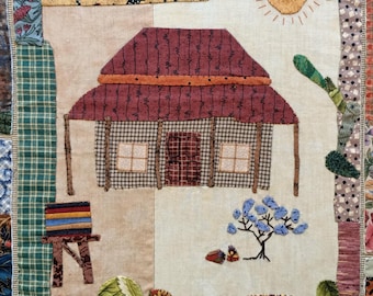 May include: A quilted wall hanging featuring a small red-roofed house with windows and a door. The house is surrounded by a variety of colourful fabric pieces, including a blue sky, green grass, and a yellow sun.