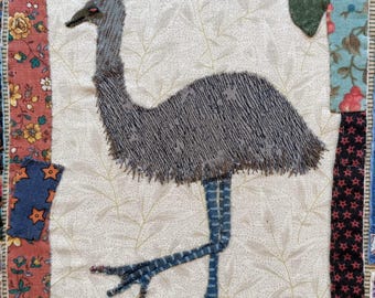 May include: An embroidered emu with a long neck and legs, standing on a green patch of grass. The emu is grey and blue, and is surrounded by a white background with a floral pattern.