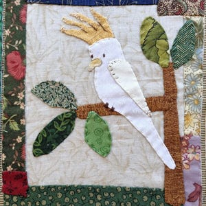 Peut inclure: Un cacatoès blanc avec une crête jaune perché sur une branche brune avec des feuilles vertes. L'oiseau est assis sur un fond de tissu blanc.