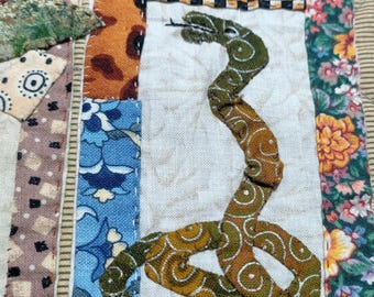 May include: A patchwork quilt featuring a green snake design in the centre. The quilt is made from various fabrics with floral and geometric patterns in shades of blue, red, green, brown and yellow.