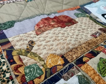 May include: A colourful patchwork quilt featuring a variety of fabrics and patterns, including a brown and white fabric with a grass-like design, a red and brown fabric with a mushroom-like design, and a blue and white fabric with a floral design.