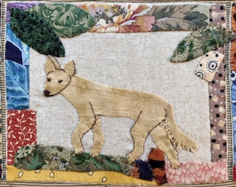 May include: A beige fabric dog with a long tail, stitched onto a white background. The dog is surrounded by a patchwork border of colourful fabric scraps.
