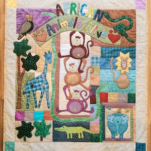 May include: A colorful patchwork quilt featuring appliqued African animals. The quilt includes a giraffe, monkeys, a lion, an elephant, and a crocodile. The words "African Animals Alive" are stitched across the top.