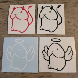 May include: Four stickers featuring a cartoon character with different expressions. The character is depicted as both an angel and a devil. The stickers are on a wooden surface.