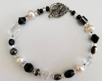 May include: A black and white beaded bracelet with a silver clasp. The bracelet features black onyx, white pearls, clear crystals, and silver beads.