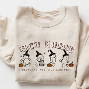 May include: A beige sweatshirt with the text "NICU NURSE" in brown letters and a graphic of four Winnie the Pooh bears wearing witch hats and holding pumpkins. The text "NEONATAL INTENSIVE CARE UNIT" is printed below the graphic.