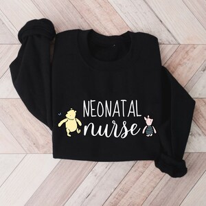 May include: Black sweatshirt with the text "NEONATAL nurse" in white lettering. A yellow cartoon bear and a pink cartoon pig are on either side of the text.