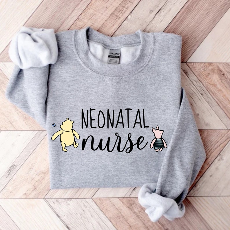 May include: Gray sweatshirt with the text "NEONATAL nurse" in black. The text is surrounded by a yellow bear and a pink pig wearing a striped bathing suit.