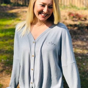 May include: A gray waffle knit button-down shirt with a tie at the waist. The shirt has the name "Karen" embroidered on the front.