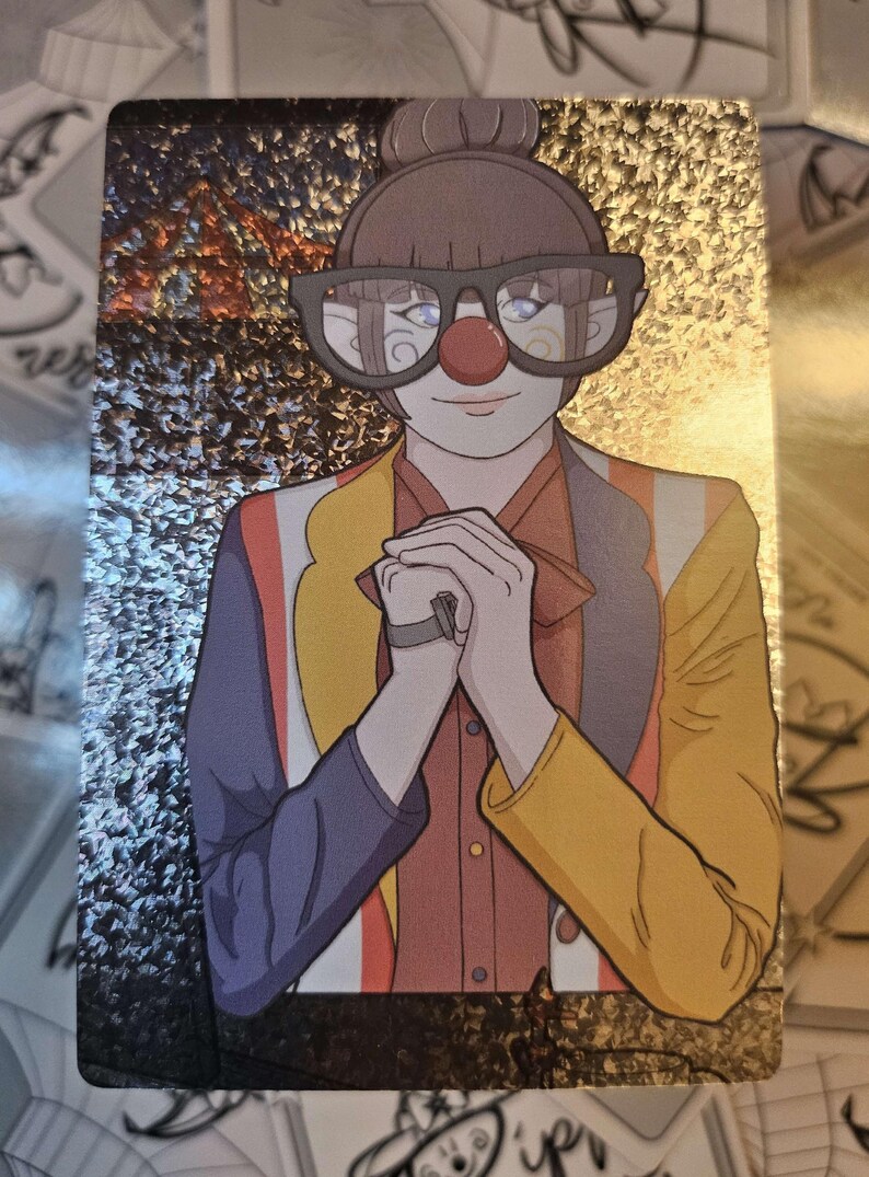 Peut inclure: Une carte &agrave; collectionner holographique rectangulaire illustrant un personnage avec un nez de clown rouge, des lunettes &agrave; monture fonc&eacute;e et les cheveux en chignon. Le personnage porte une veste multicolore aux panneaux violets, jaunes et orange.