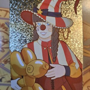Peut inclure: Une carte &agrave; collectionner holographique rectangulaire repr&eacute;sentant un personnage d&eacute;guis&eacute; en clown avec un chapeau et une cape &agrave; rayures rouges et blanches. Le personnage a des cheveux tress&eacute;s, un nez rouge et tient un ballon en forme de chien.