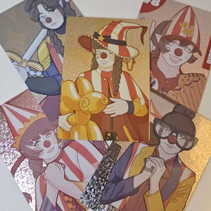 Peut inclure: Une collection de cinq cartes &agrave; collectionner rectangulaires illustrant des personnages au maquillage de clown, incluant des nez rouges. Les cartes pr&eacute;sentent diverses tenues, des chapeaux ray&eacute;s et un ballon animal jaune, avec des finitions m&eacute;tallis&eacute;es.