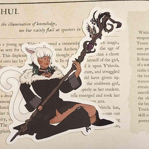 May include: A die-cut sticker featuring a character with white hair and cat-like ears, wearing a black outfit with a fur collar, holding a dark, ornate staff with a purple gem. The sticker is placed over a page of text titled Y'shtola Rhul.
