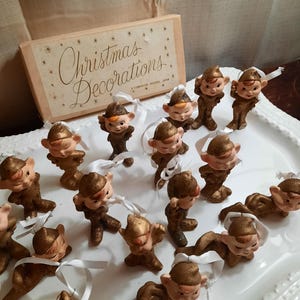 May include: A set of 18 gold glitter Christmas elf ornaments with white ribbon hangers. The ornaments are in a vintage style and come in a box that says "Christmas Decorations".