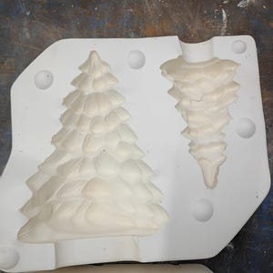 May include: A white mold with two Christmas tree-shaped cavities. One cavity is a complete tree, the other is a tree ornament. The mold is made of a durable material, perfect for crafting holiday decorations.