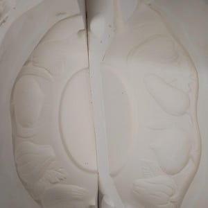 May include: A two-piece white ceramic slip casting mold featuring an embossed fruit and vegetable motif. The interior surfaces display recessed carvings of pears, apples, and leafy stems, designed to create a detailed relief pattern on cast items.
