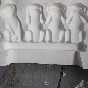 May include: A white plaster sculpture depicting the three wise monkeys: see no evil, hear no evil, speak no evil. The monkeys are seated on a white base. The sculpture is in a mold.