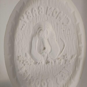 May include: An oval white ceramic mold featuring a relief sculpture of a basset hound dog. The text "CHON BABY" is embossed at the top and "LES BOOGIES" is embossed at the bottom. The background has a textured, vertical line pattern.