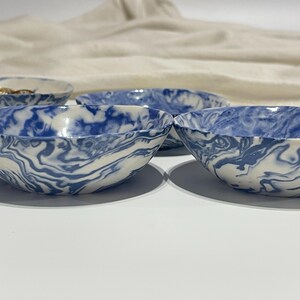 May include: Four small ceramic bowls with a blue and white marbled design. The bowls are arranged in a row, with the front bowl slightly offset from the others.
