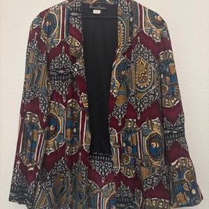 May include: A burgundy, blue, gold, and black patterned blazer with a black lining. The label reads "Bertie Stephens".