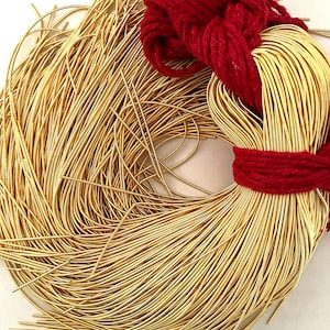 Puede incluir: Una gran bobina de alambre de color dorado, envuelta alrededor de un cordón rojo. El alambre es delgado y flexible, y es perfecto para hacer joyas u otros proyectos.