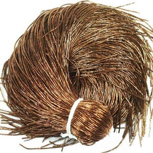 Puede incluir: Un paquete de cordón metálico dorado y marrón, atado con una cinta blanca. El cordón es brillante y tiene un ligero brillo.