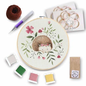 Puede incluir: Un kit de bordado de punto de cruz con un lindo erizo que lleva una corona de flores y está rodeado de vegetación. El kit incluye hilo de bordar, una aguja, un aro y instrucciones.