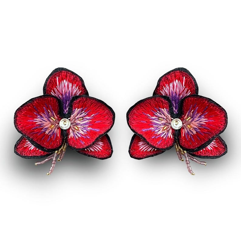 May include: A pair of red and purple embroidered flower earrings with a clear rhinestone center.