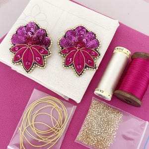Puede incluir: Dos broches florales hechos a mano con lentejuelas en tonos fucsia y morado, con ribete dorado. La imagen también muestra carretes de hilo, cuentas doradas y alambre dorado, lo que sugiere un proyecto de artesanía o bricolaje.