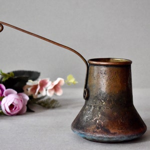May include: A vintage copper coffee pot with a long, curved handle. The pot has a worn, aged patina and a blue-green tint at the base.