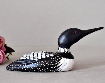 May include: A black and white wooden loon figurine with red eyes. The loon is painted with a black and white pattern of dots and stripes.