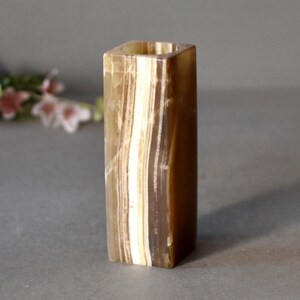 K&ouml;nnte beinhalten: Eine quadratische, braune und wei&szlig;e Onyx-Vase mit glatter, polierter Oberfl&auml;che.