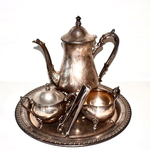 May include: A silver tea set with a teapot, creamer, sugar bowl, and tongs on a silver tray.