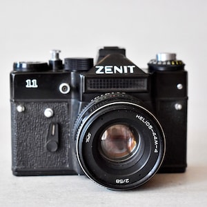 Può includere: Una macchina fotografica a pellicola Zenit 11 nera con un obiettivo Helios-44M-4.