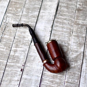 May include: A brown wooden pipe with a black stem and a metal band. The pipe is sitting on a white wooden surface.