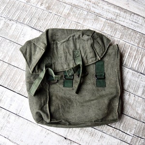 Può includere: Uno zaino militare in tela verde con spalline e fibbie regolabili.