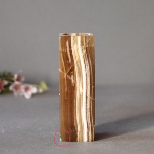 K&ouml;nnte beinhalten: Eine braune und wei&szlig;e gestreifte Onyx-Vase mit quadratischer Form. Die Vase ist aus Naturstein gefertigt und hat eine glatte, polierte Oberfl&auml;che.