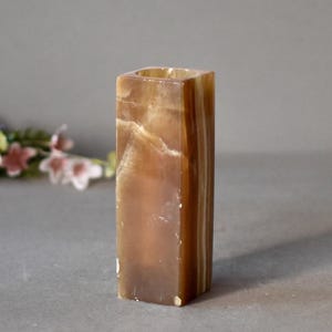 K&ouml;nnte beinhalten: Ein quadratischer Kerzenhalter aus braunem und wei&szlig;em Onyx mit einer glatten, polierten Oberfl&auml;che.