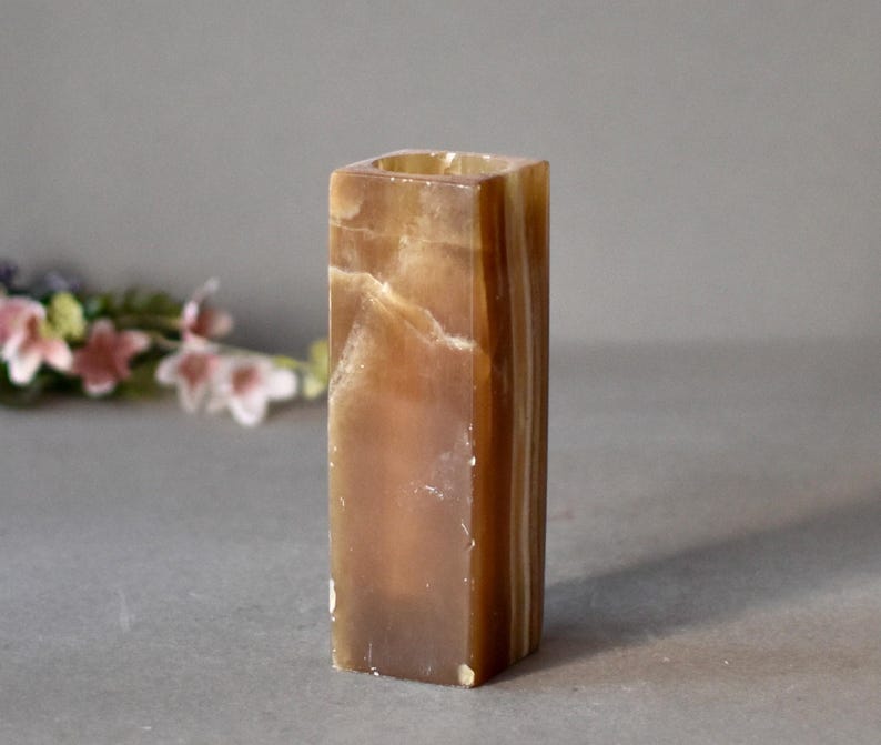 K&ouml;nnte beinhalten: Ein quadratischer Kerzenhalter aus braunem und wei&szlig;em Onyx mit einer glatten, polierten Oberfl&auml;che.